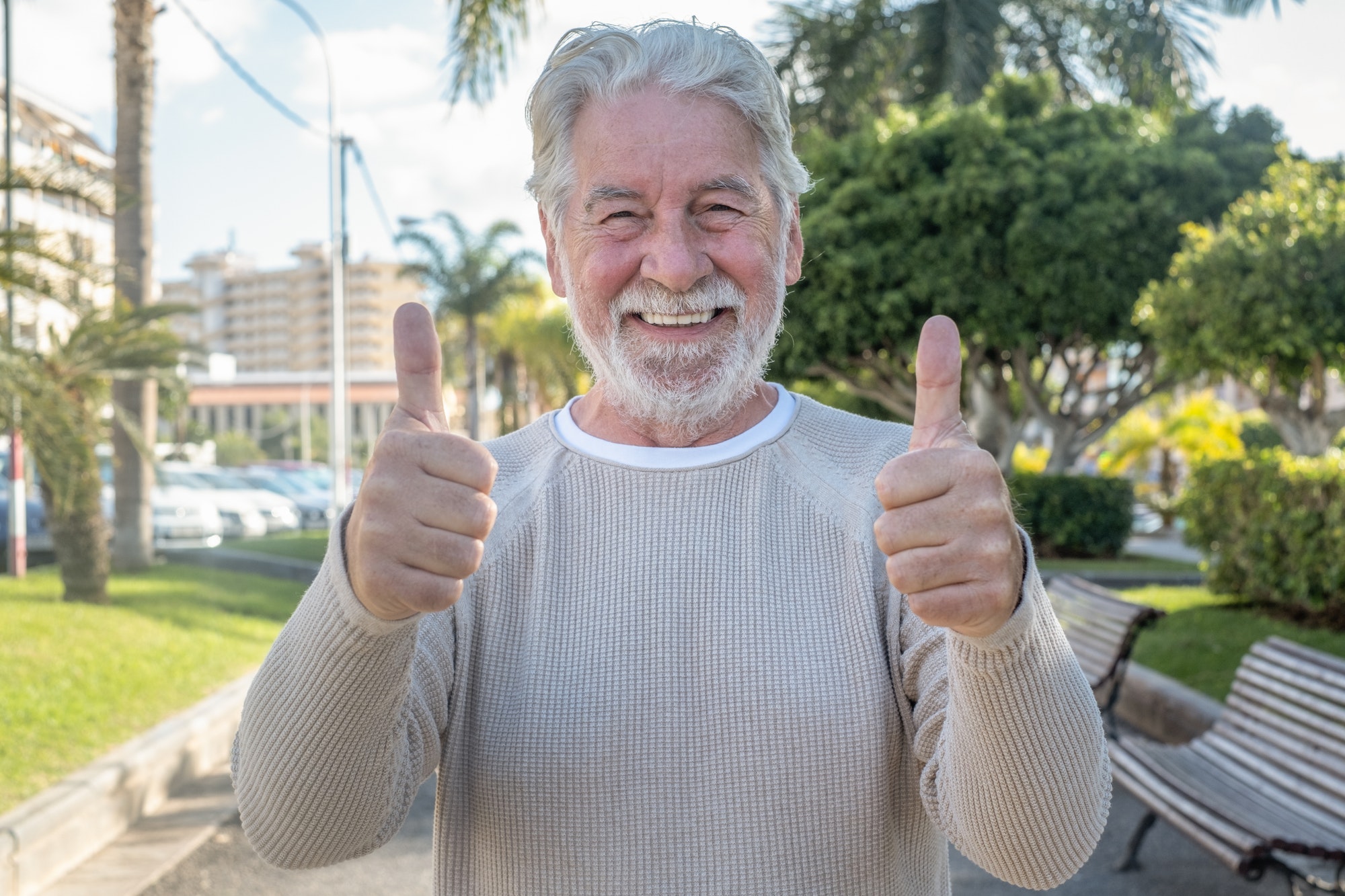 Portrait of attractive smiling senior man standing outdoor in public park with thumbs up.