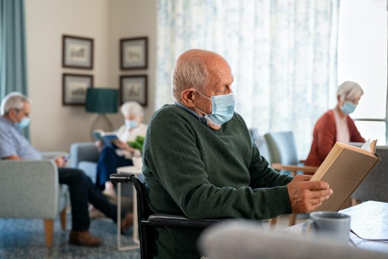 Senior man with face mask reading book at assisted living centre